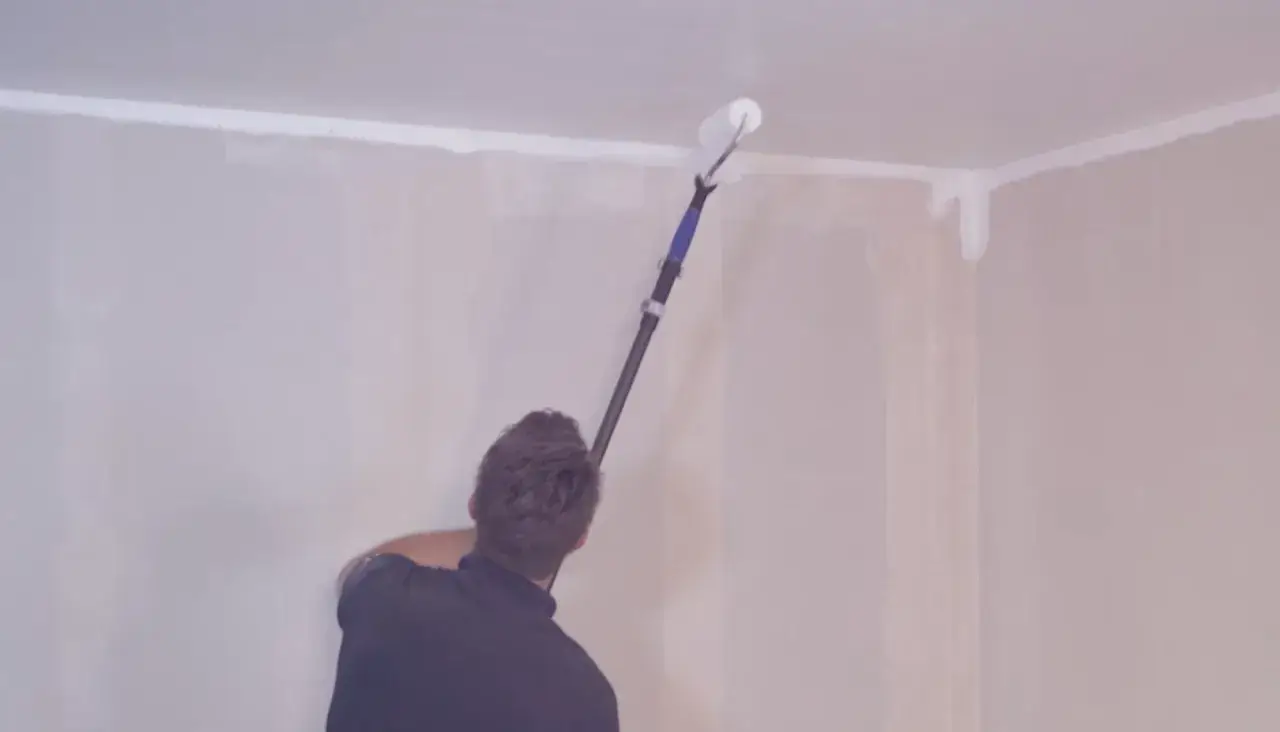 Person målar om taket med en lång roller.