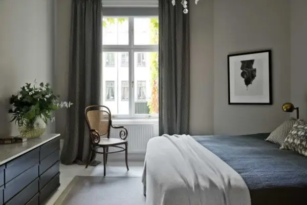 Sovrum med en säng, en stol och en byrå. Konst av Sofia Wallenstam på väggen.