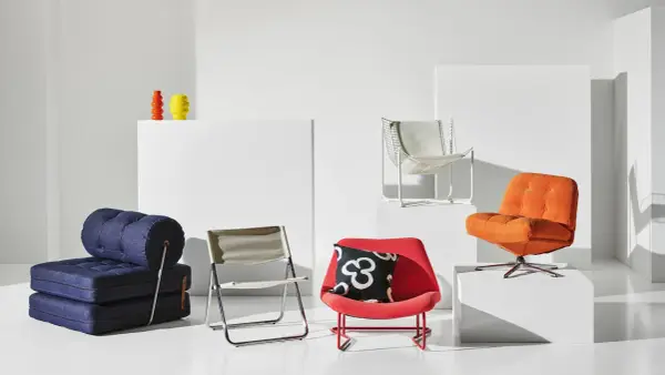 En samling möbler i 70-tals inredning: en blå bäddsoffa, en röd fåtölj med mönstrat kudde, en orange fåtölj och en vit metallstol.