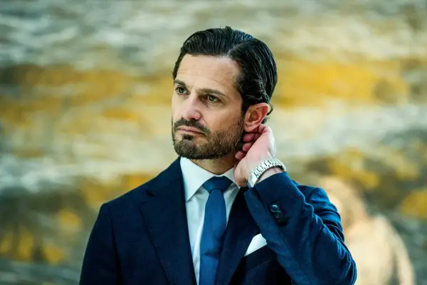 Prins Carl Philip i mörkblå kostym, vit skjorta och blå slips. Hans hand vilar bakom örat, en detalj som speglar hans intresse för carl philip design.